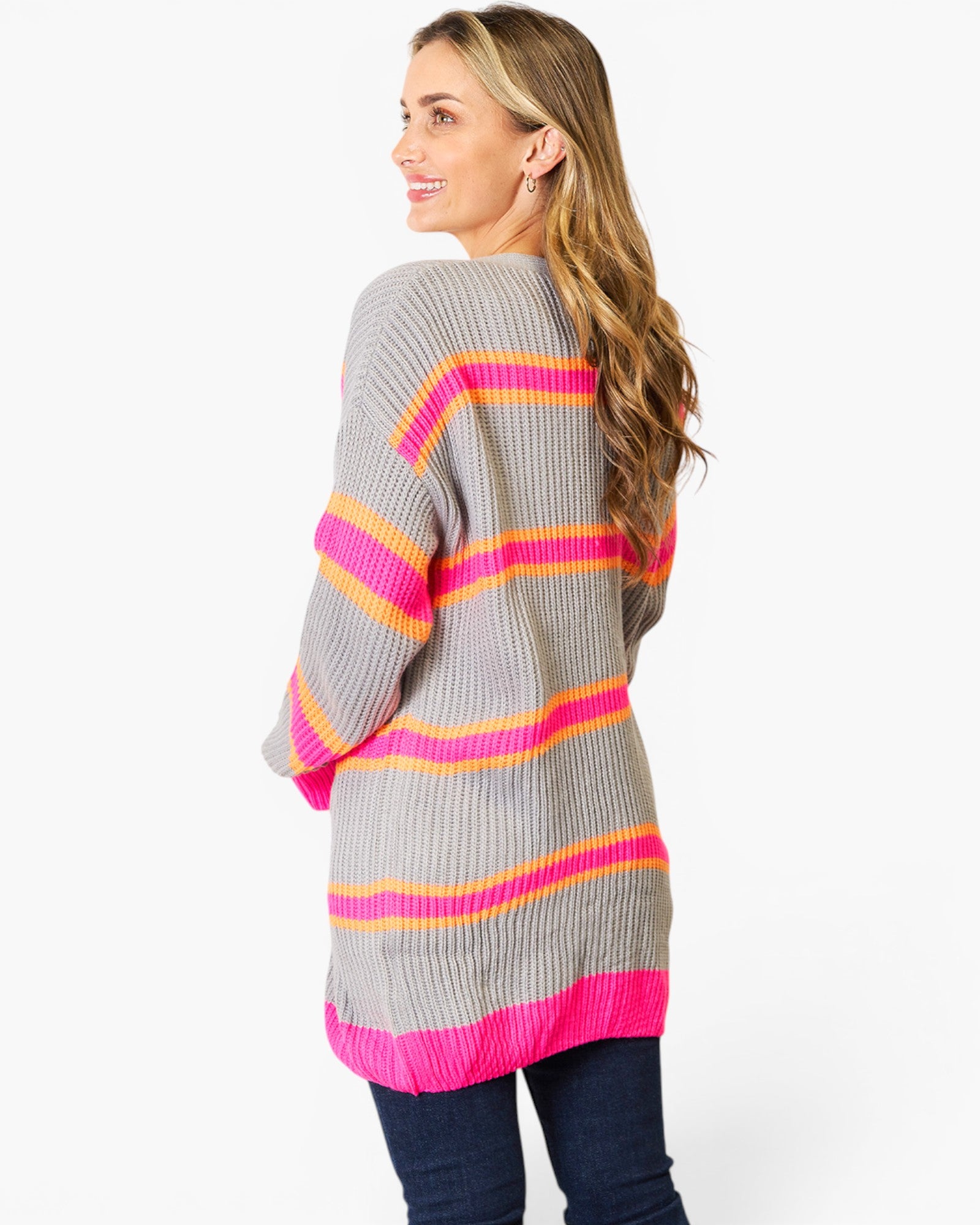 A woman shown from the back wearing a gray ribbed knit sweater with bright pink, orange, and yellow horizontal stripes, paired with dark blue jeans, against a plain white studio background.