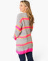 A woman shown from the back wearing a gray ribbed knit sweater with bright pink, orange, and yellow horizontal stripes, paired with dark blue jeans, against a plain white studio background.