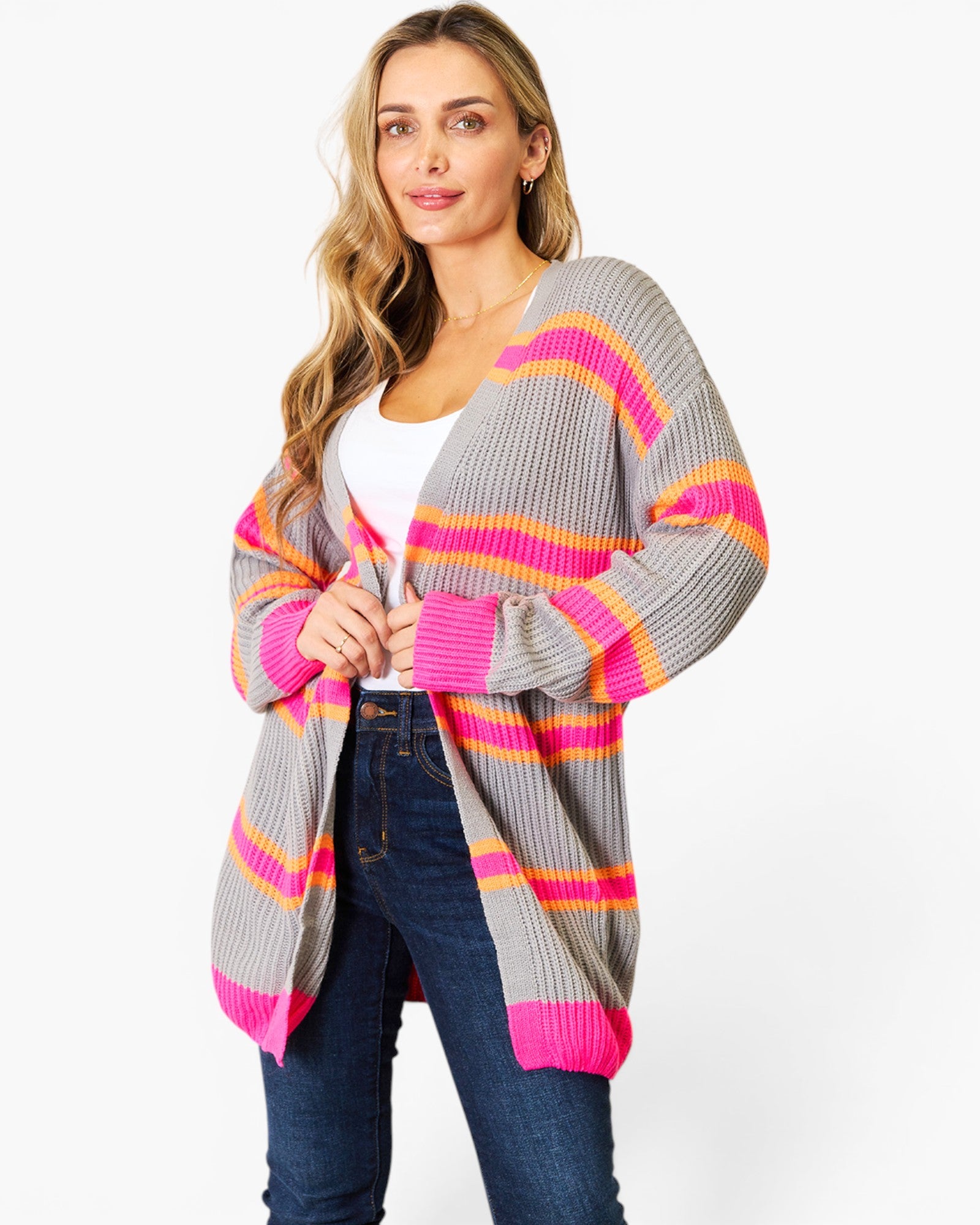 A woman wearing a gray open-front cardigan with bright pink, orange, and yellow horizontal stripes, styled with a white top and dark blue jeans against a plain white background.