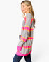 A woman wearing a gray ribbed knit cardigan with bright pink and orange horizontal stripes, paired with a white top and dark blue jeans, photographed against a plain white studio background.