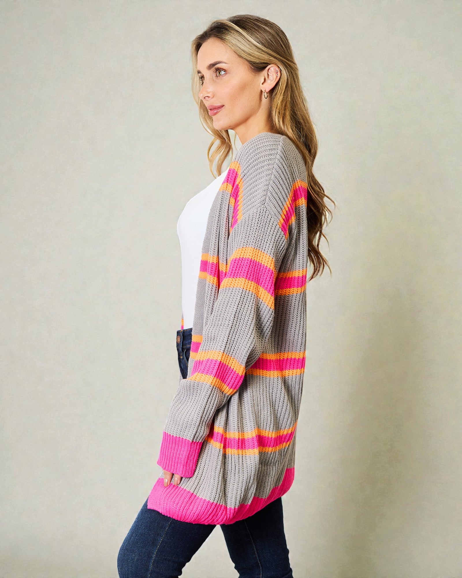 Woman wearing a gray cardigan with pink and orange stripes on a plain background