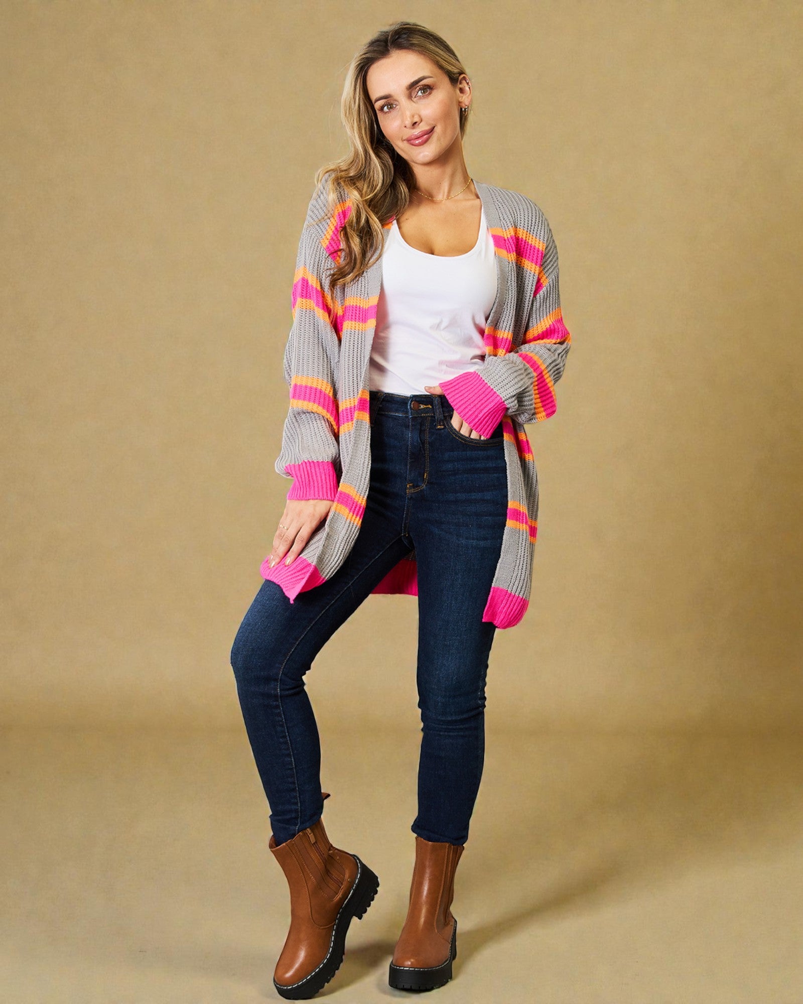 Woman wearing a colorful cardigan, white top, blue jeans, and brown boots on a beige background