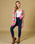 Woman wearing a colorful cardigan, white top, blue jeans, and brown boots on a beige background