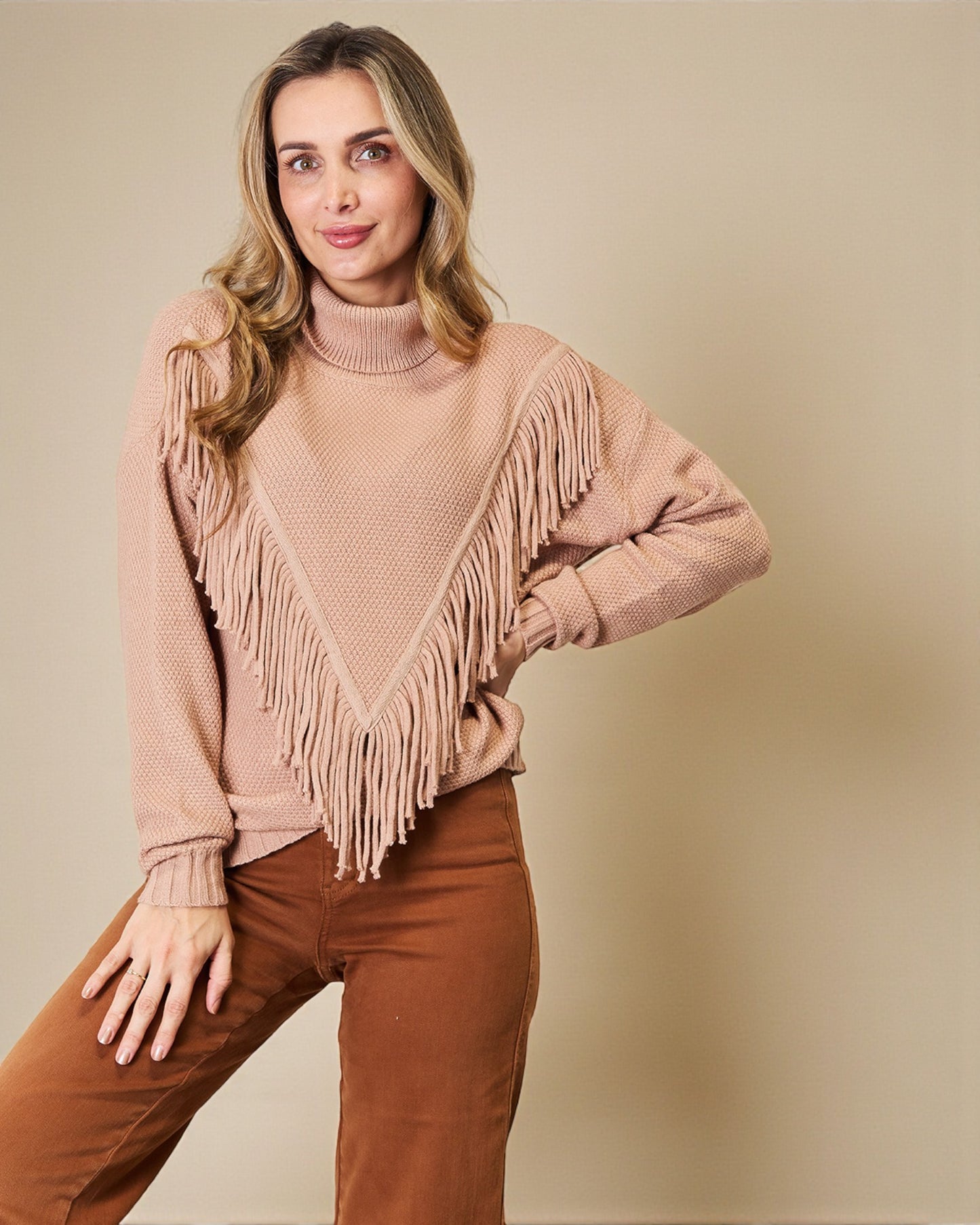 Woman wearing a beige sweater with fringe details against a beige background