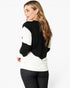 A woman wearing a black and white color-block knit sweater, shown from a rear three-quarter angle against a plain white studio background.