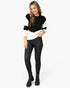 A woman modeling a colorblock knit sweater with black and white sections, paired with black skinny pants and black ankle boots, against a plain white studio background.