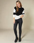 Woman wearing a black and white sweater with black pants on a beige background