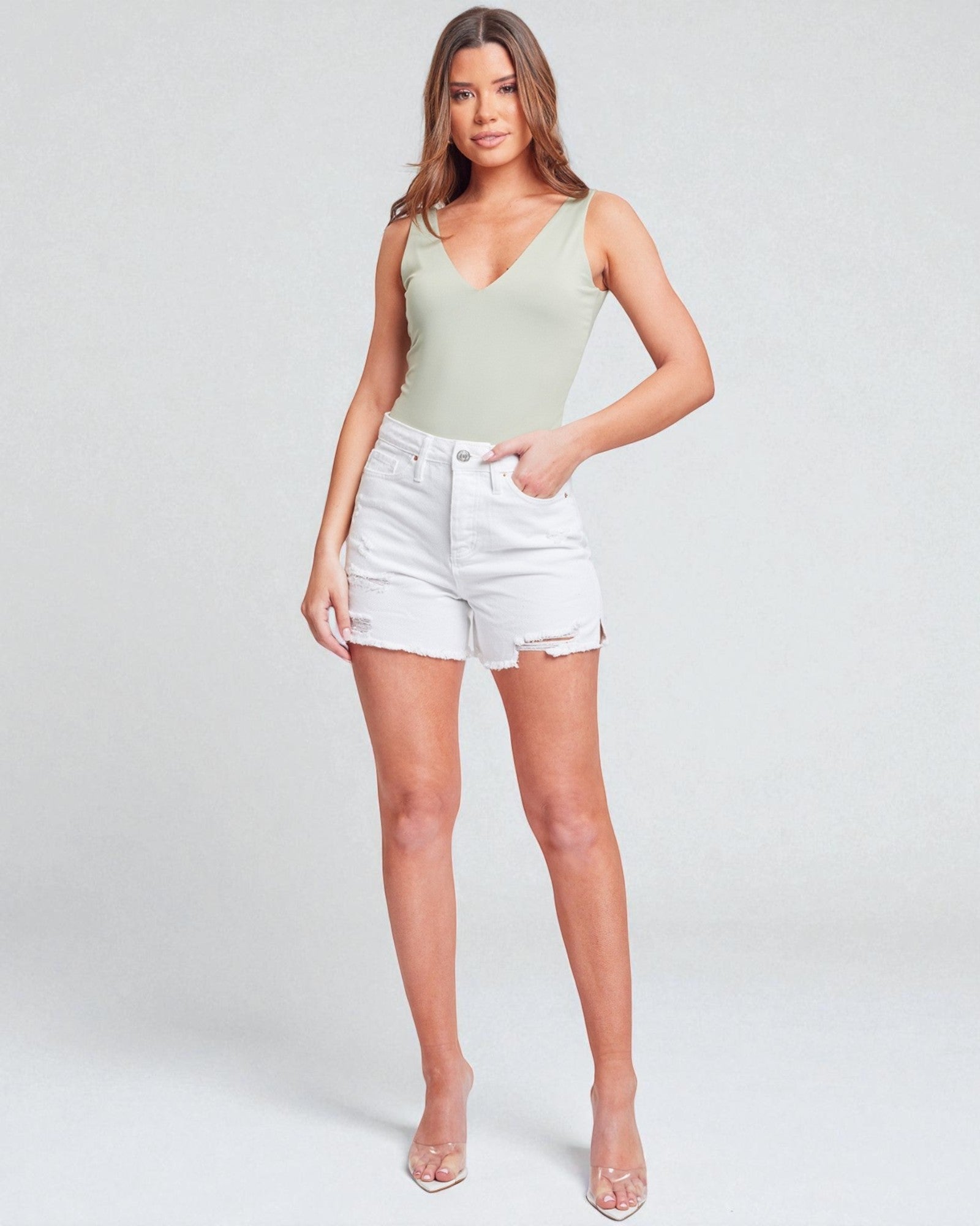 Woman wearing a light green tank top and white shorts on a plain background