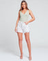 Woman wearing a light green tank top and white shorts on a plain background