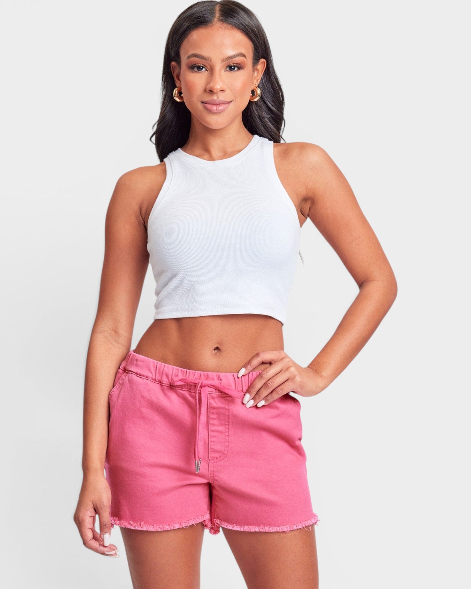 Woman wearing a white crop top and pink shorts on a light gray background