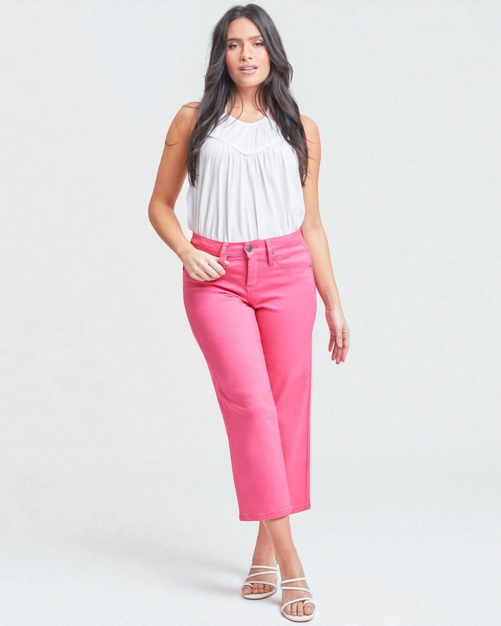 Woman wearing a white sleeveless top and bright pink pants on a white background