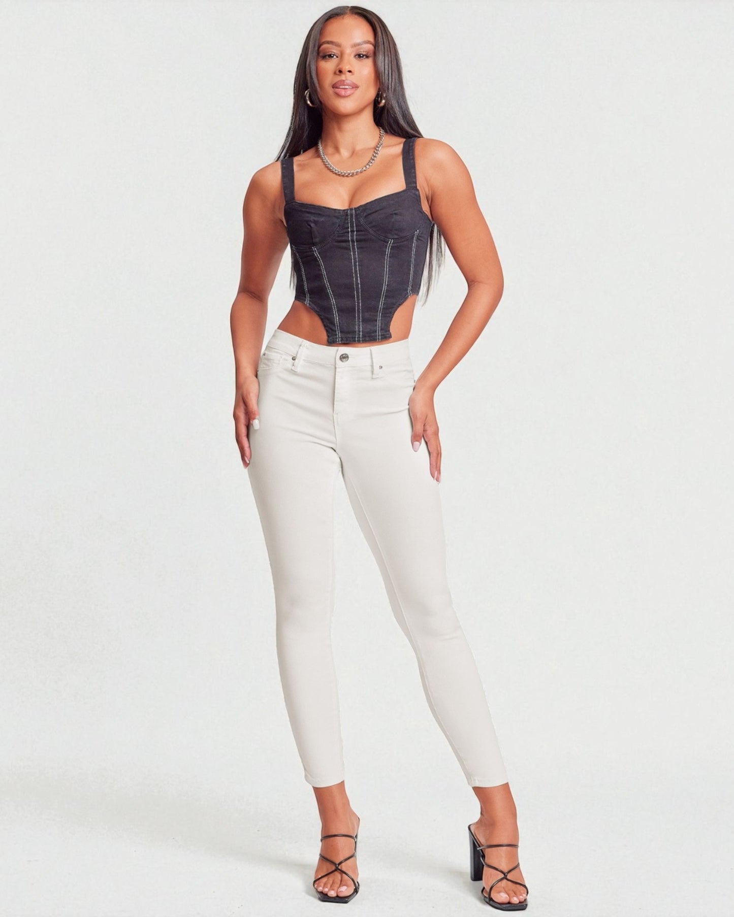 Woman wearing a denim corset top and white pants on a plain background
