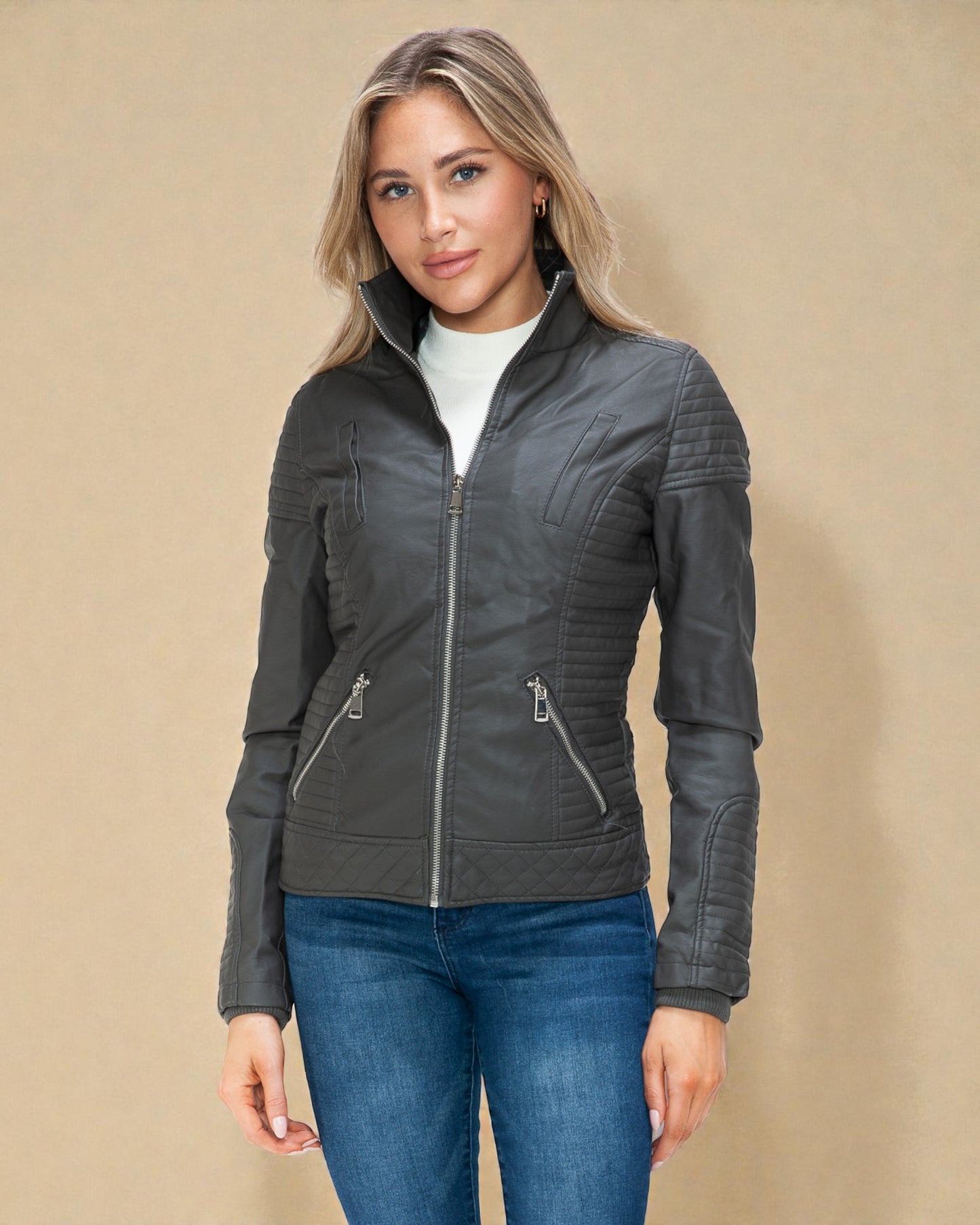 Woman wearing a gray quilted jacket and blue jeans on a beige background