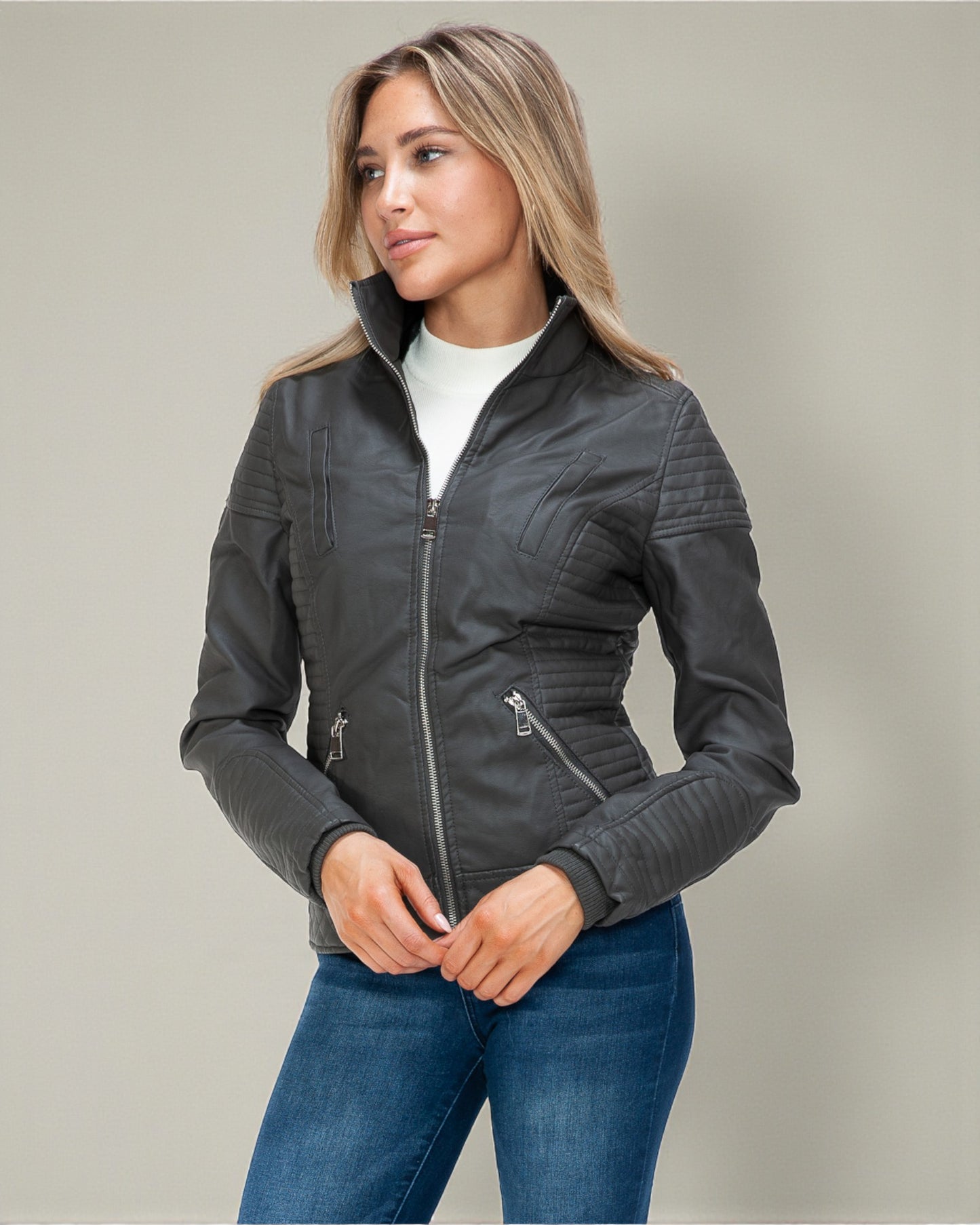 Woman wearing a gray jacket and blue jeans against a neutral background