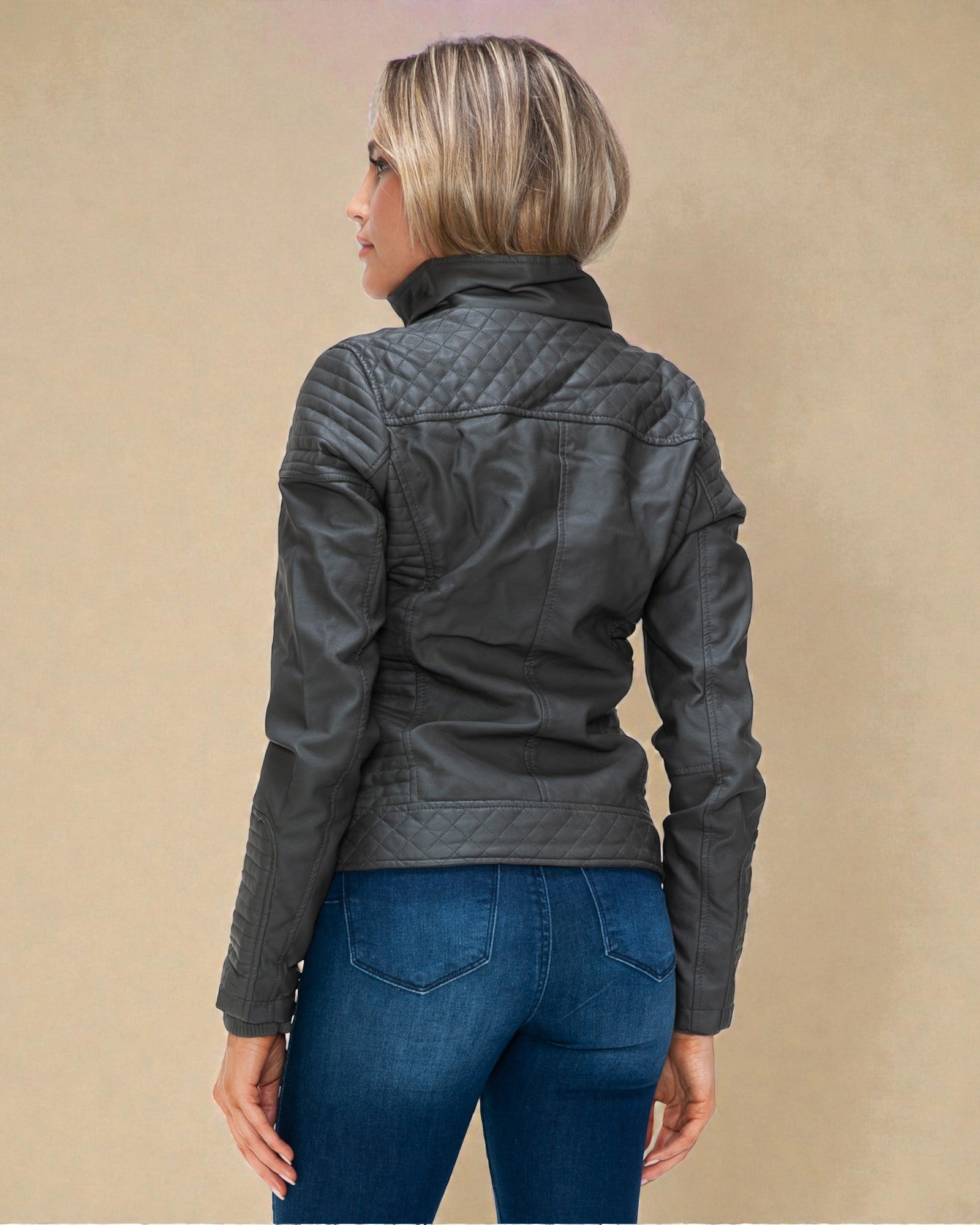 Person wearing a dark quilted jacket and blue jeans on a beige background