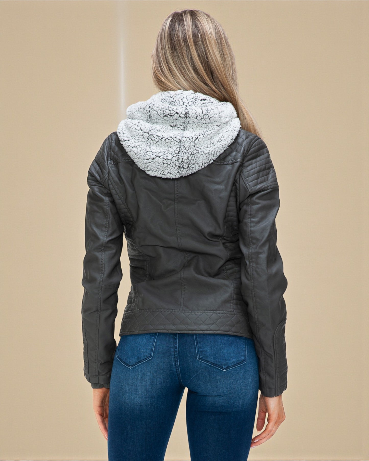 Person wearing a black leather jacket with a fur-lined hood on a beige background