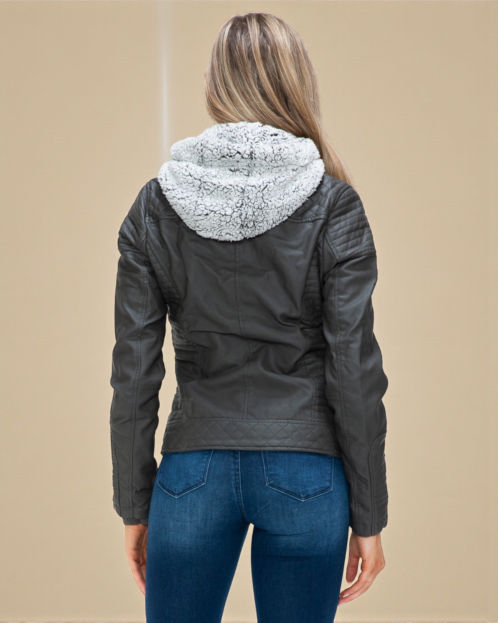 Person wearing a black leather jacket with a fur-lined hood on a beige background