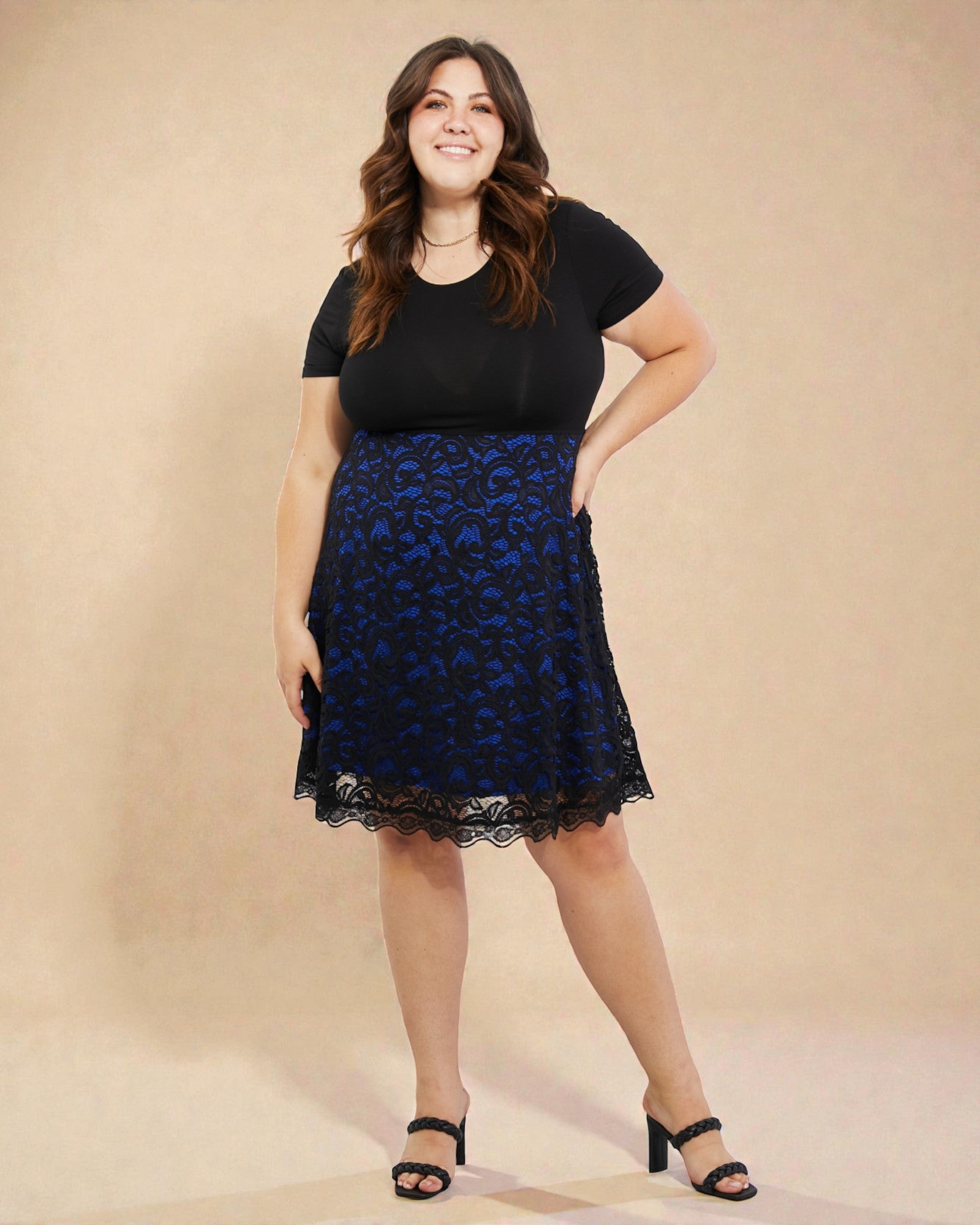 Woman wearing a black top and blue lace skirt on a beige background