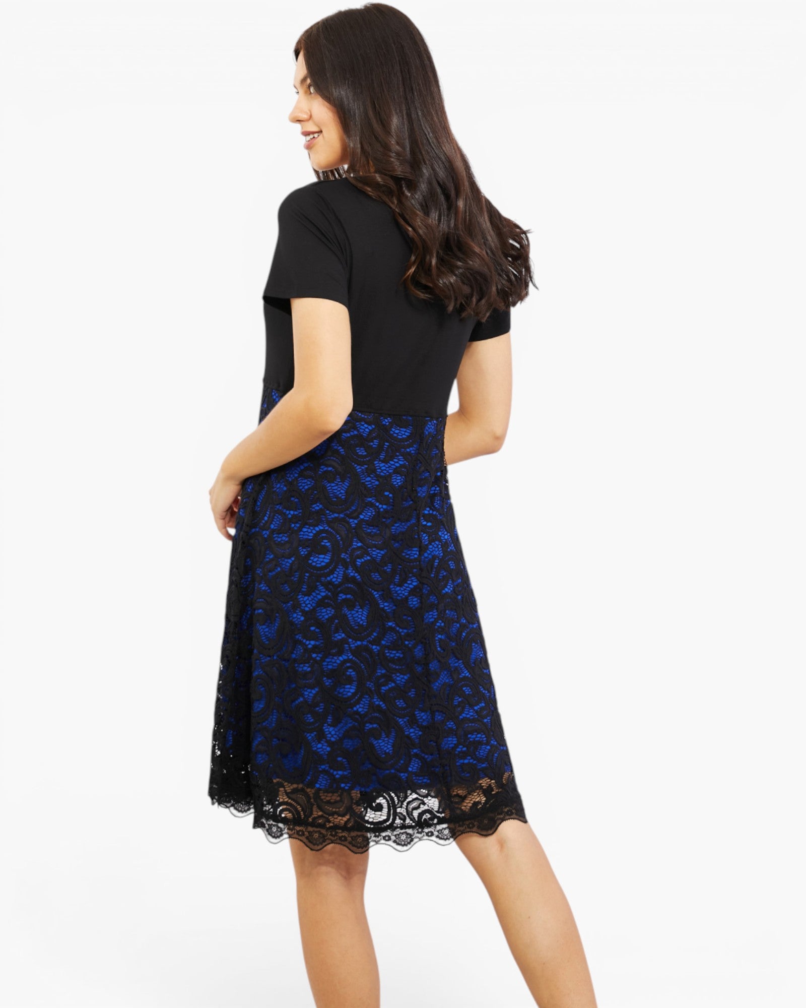 A woman shown from the back wearing a short-sleeve black top and a knee-length blue and black floral lace skirt against a plain white studio background.