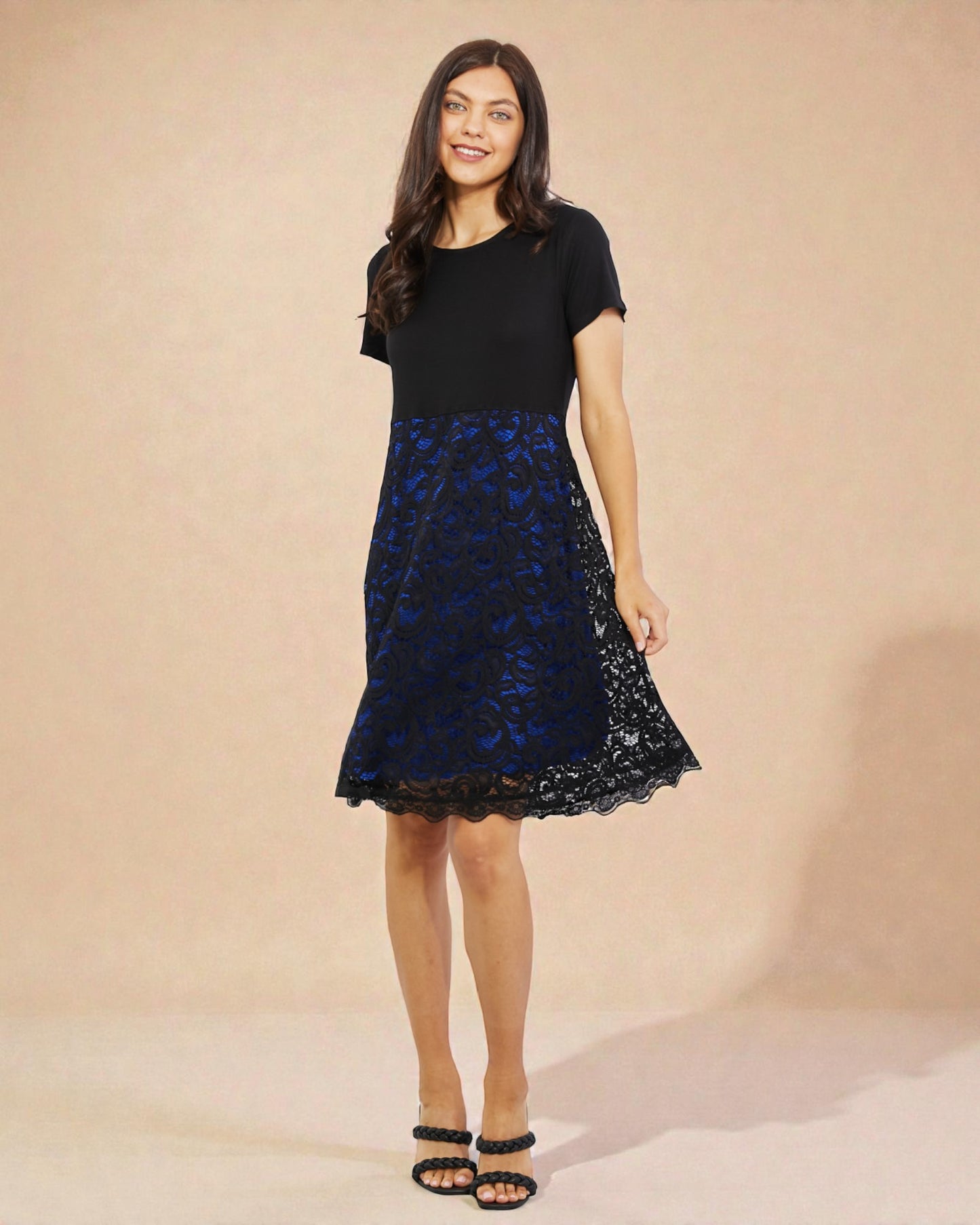 Woman wearing a black dress with a blue lace overlay against a beige background