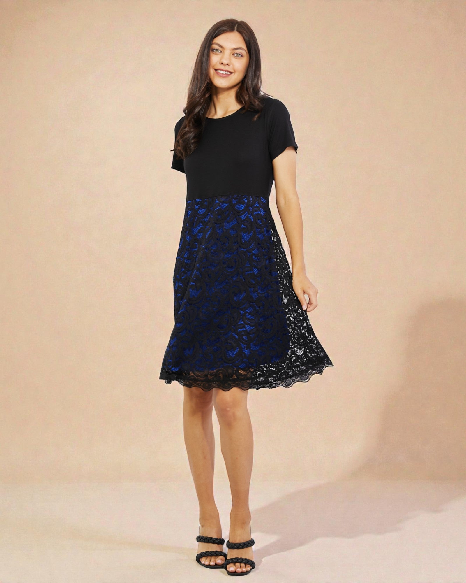 Woman wearing a black dress with a blue lace overlay against a beige background