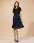 Woman wearing a black dress with a blue lace overlay against a beige background