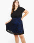 A woman modeling a black short-sleeve top paired with a black and royal blue patterned lace skirt against a plain white background.