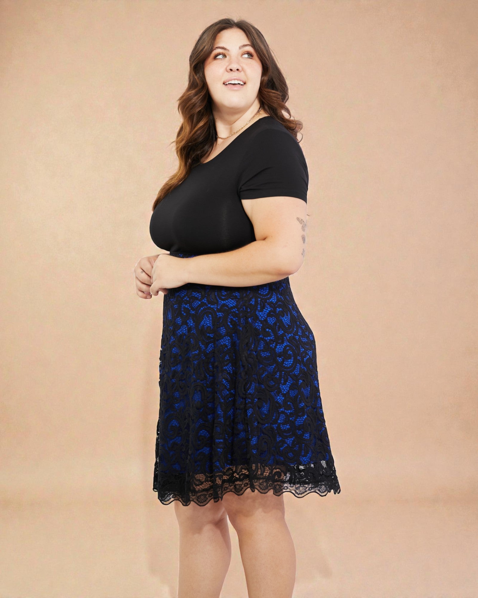 Woman wearing a black top and blue lace skirt against a beige background