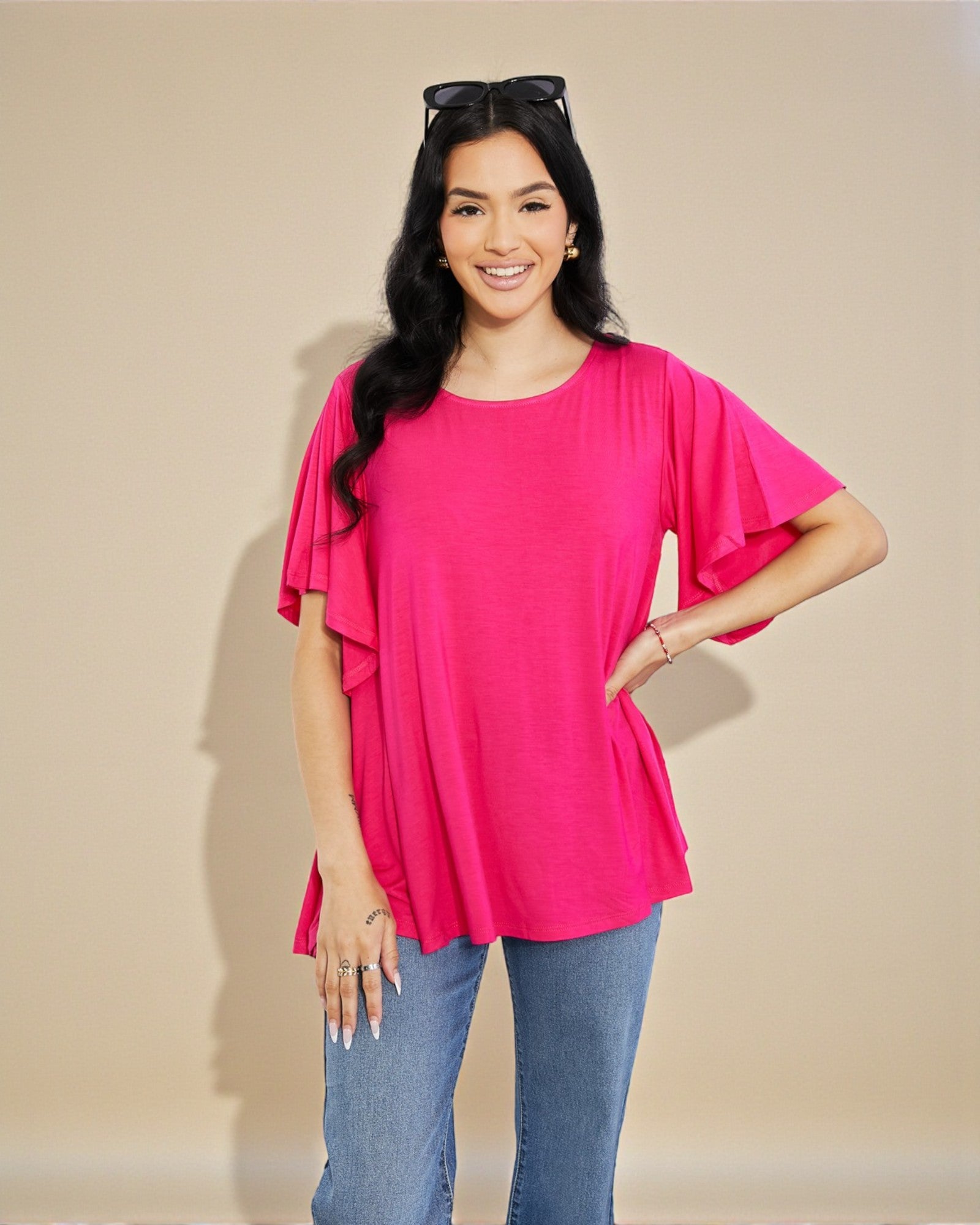 Woman wearing a bright pink blouse with ruffled sleeves against a beige background