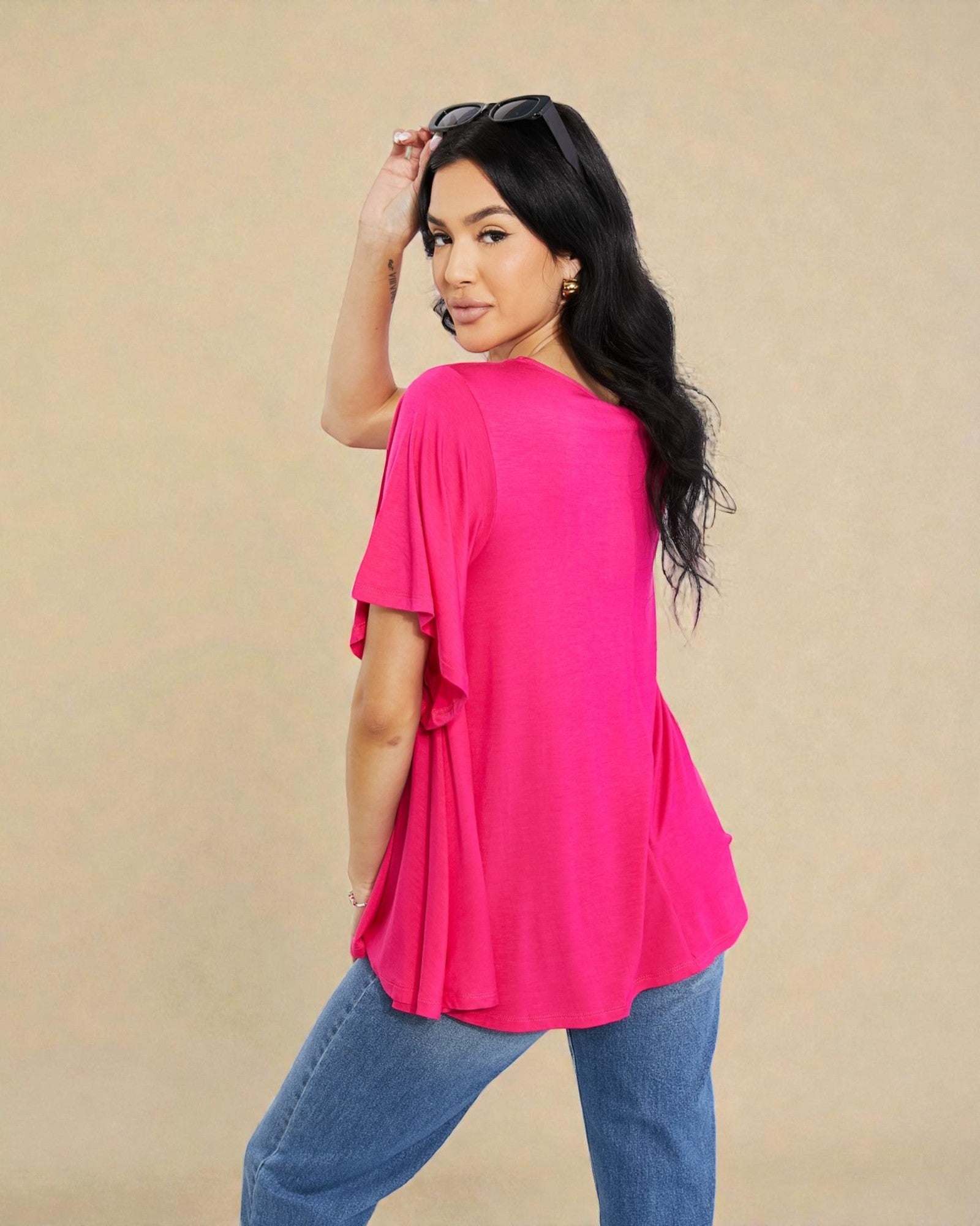 Woman wearing a bright pink top and blue jeans against a beige background