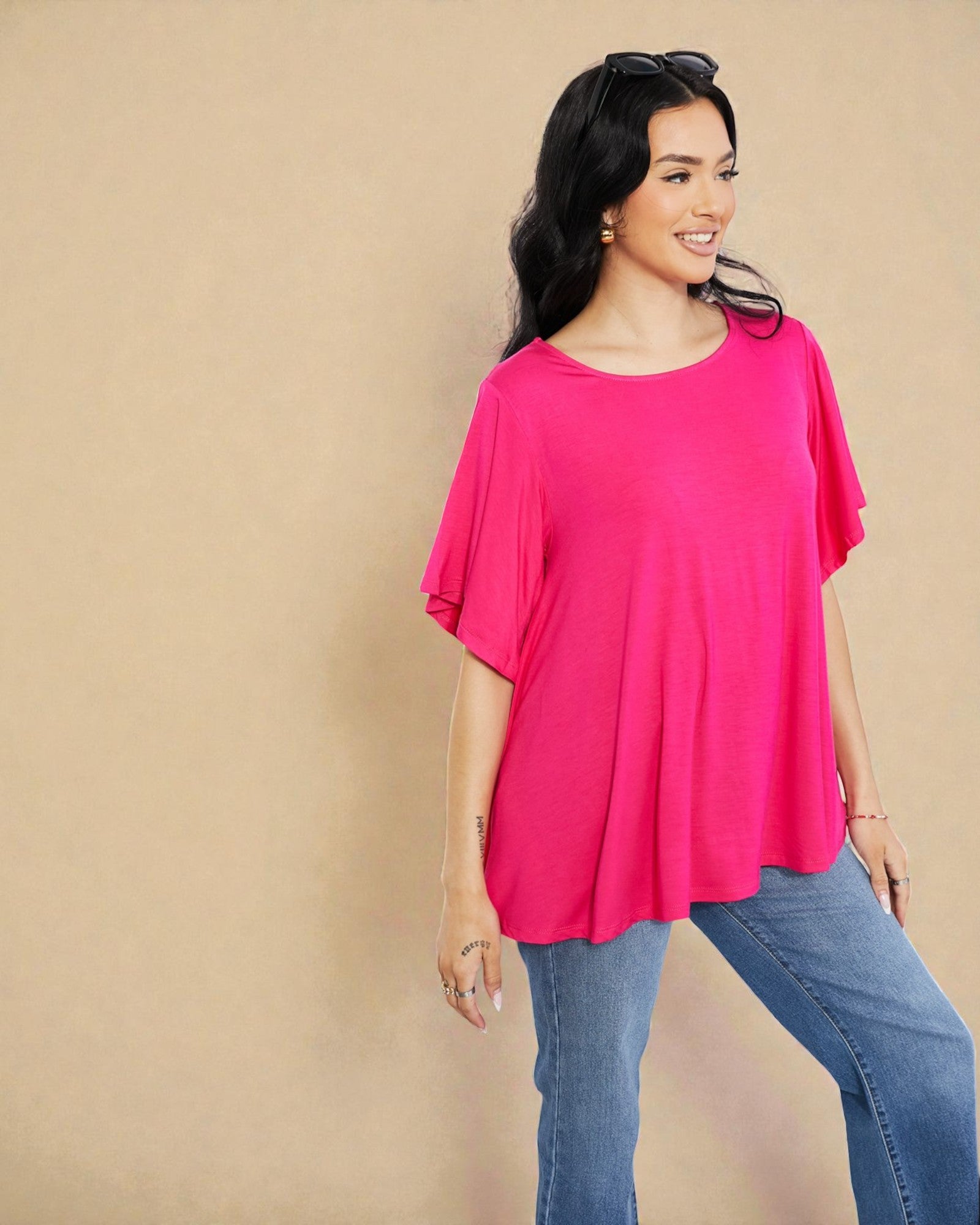 Woman wearing a bright pink top and blue jeans against a beige background