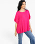 A woman wearing a bright hot pink short-sleeve tunic top with layered ruffle details on the sleeves, paired with blue jeans, photographed against a solid white studio background.
