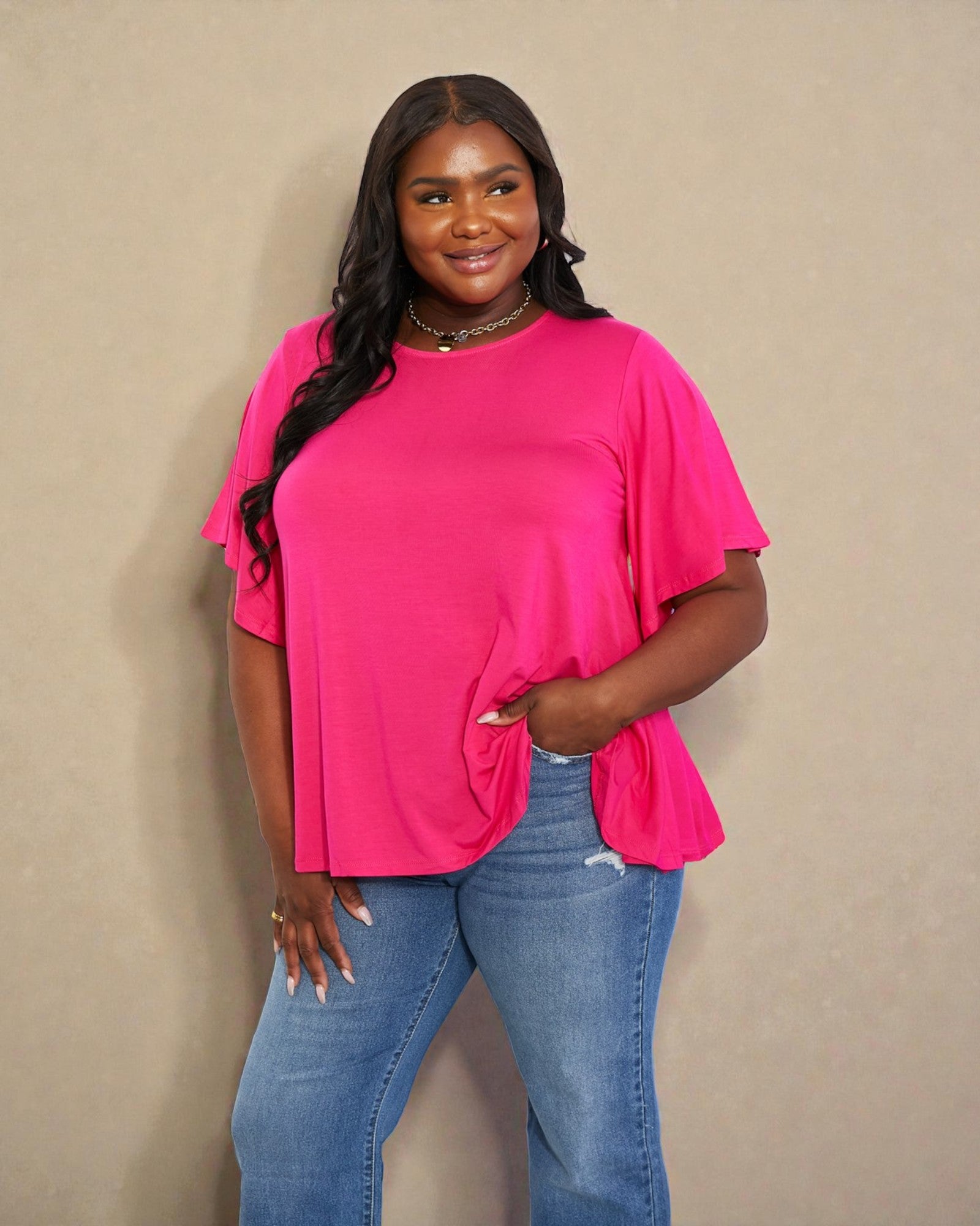 Woman wearing a bright pink top and blue jeans against a beige background