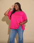 Woman wearing a bright pink top and blue jeans against a beige background