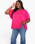 A woman modeling a bright hot pink short-sleeve top with a relaxed, slightly oversized fit and side pockets, paired with blue jeans, against a plain white studio background.