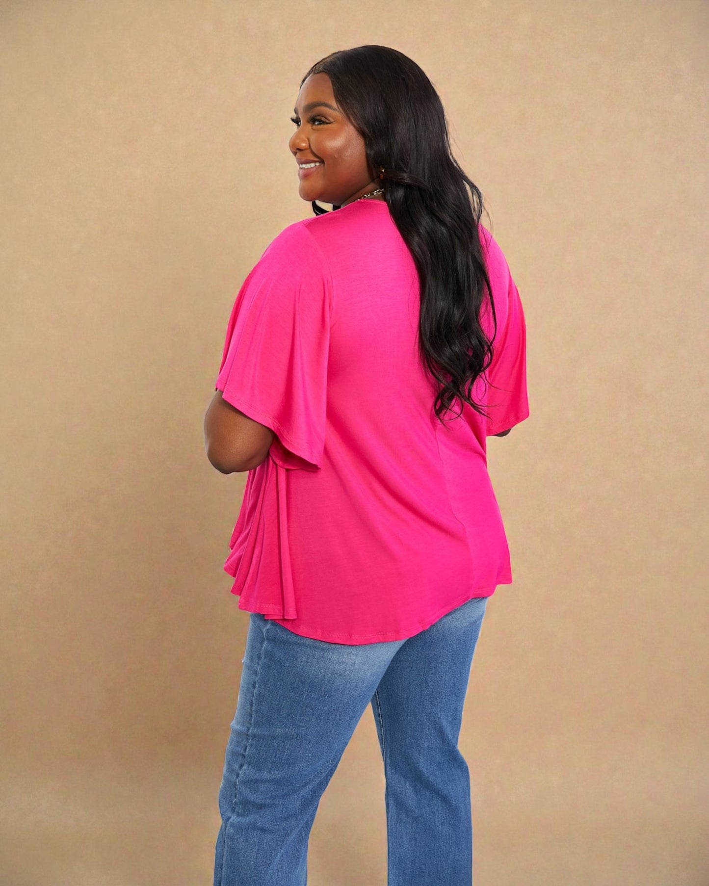 Woman wearing a bright pink top and blue jeans against a beige background