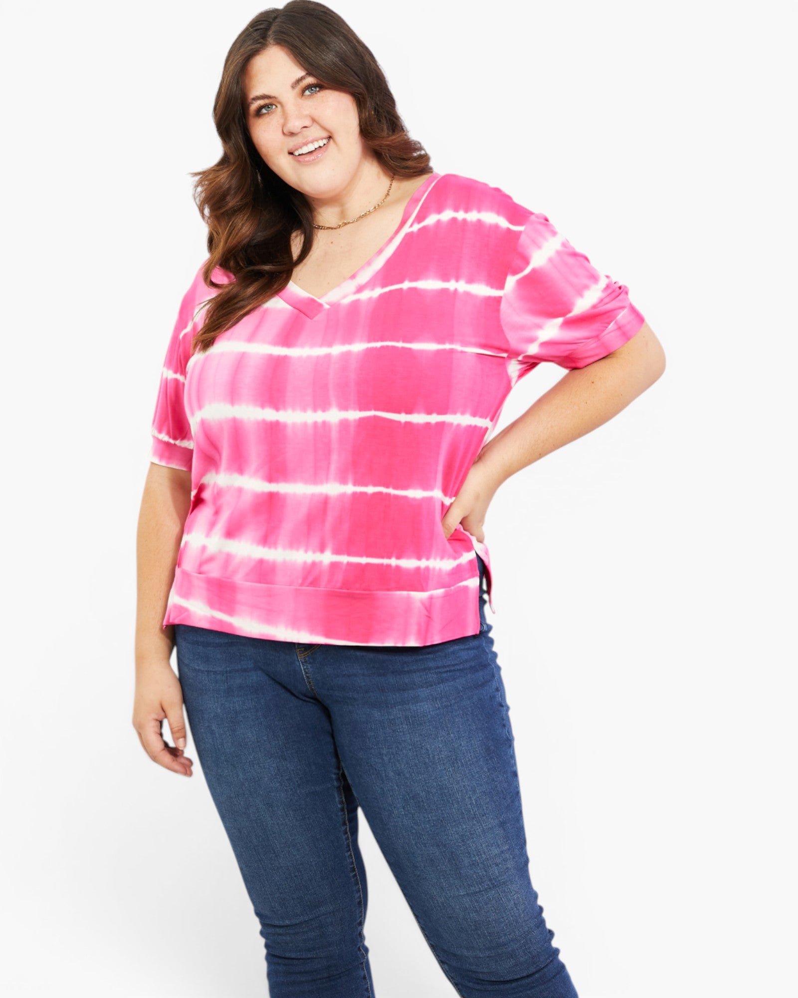 A woman modeling a pink and white tie-dye short-sleeve top with blue jeans against a plain white background.