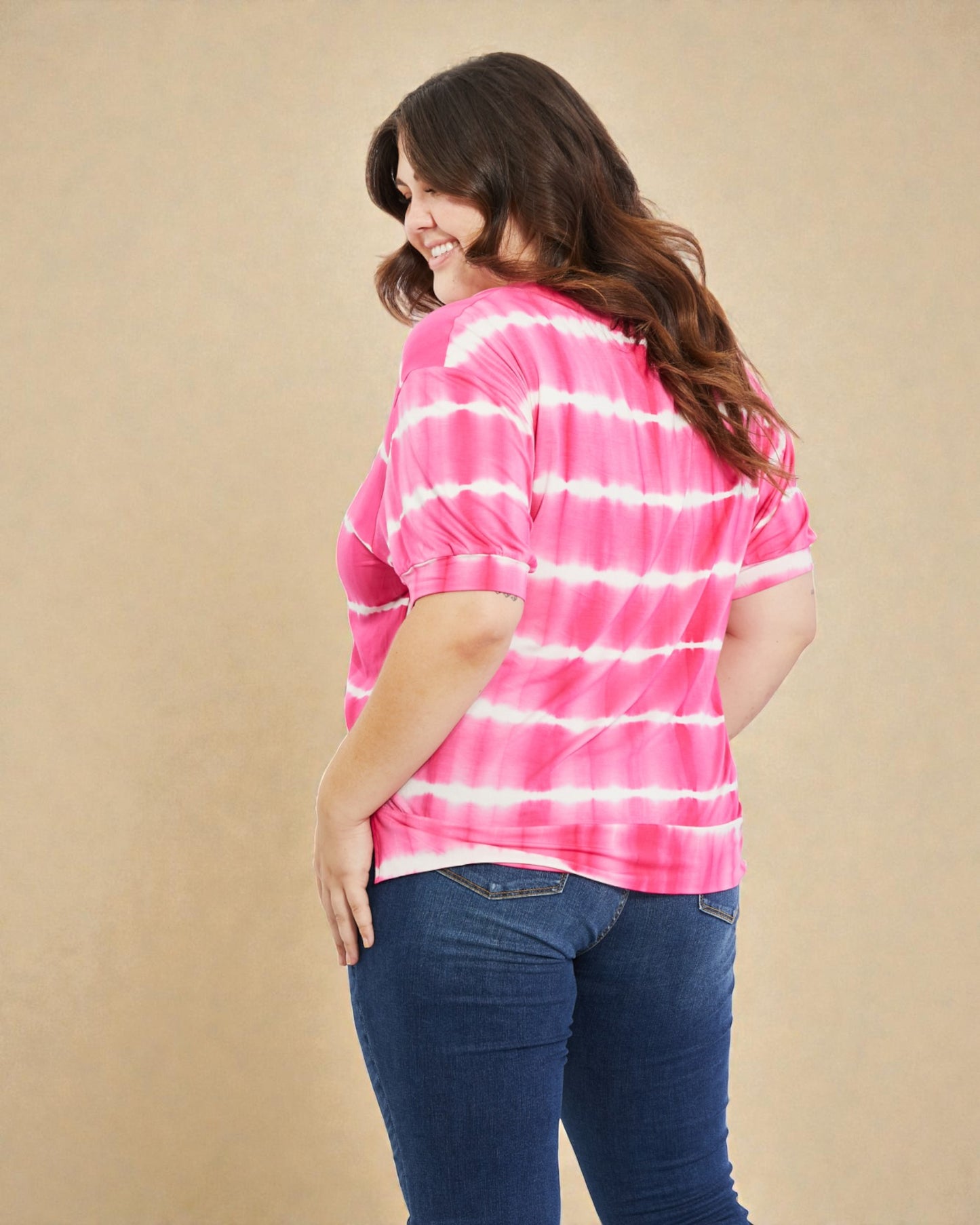Woman wearing a pink and white tie-dye shirt with blue jeans on a beige background