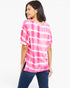 A woman wearing a pink and white tie-dye short-sleeve top and dark blue jeans, photographed against a plain white studio background.