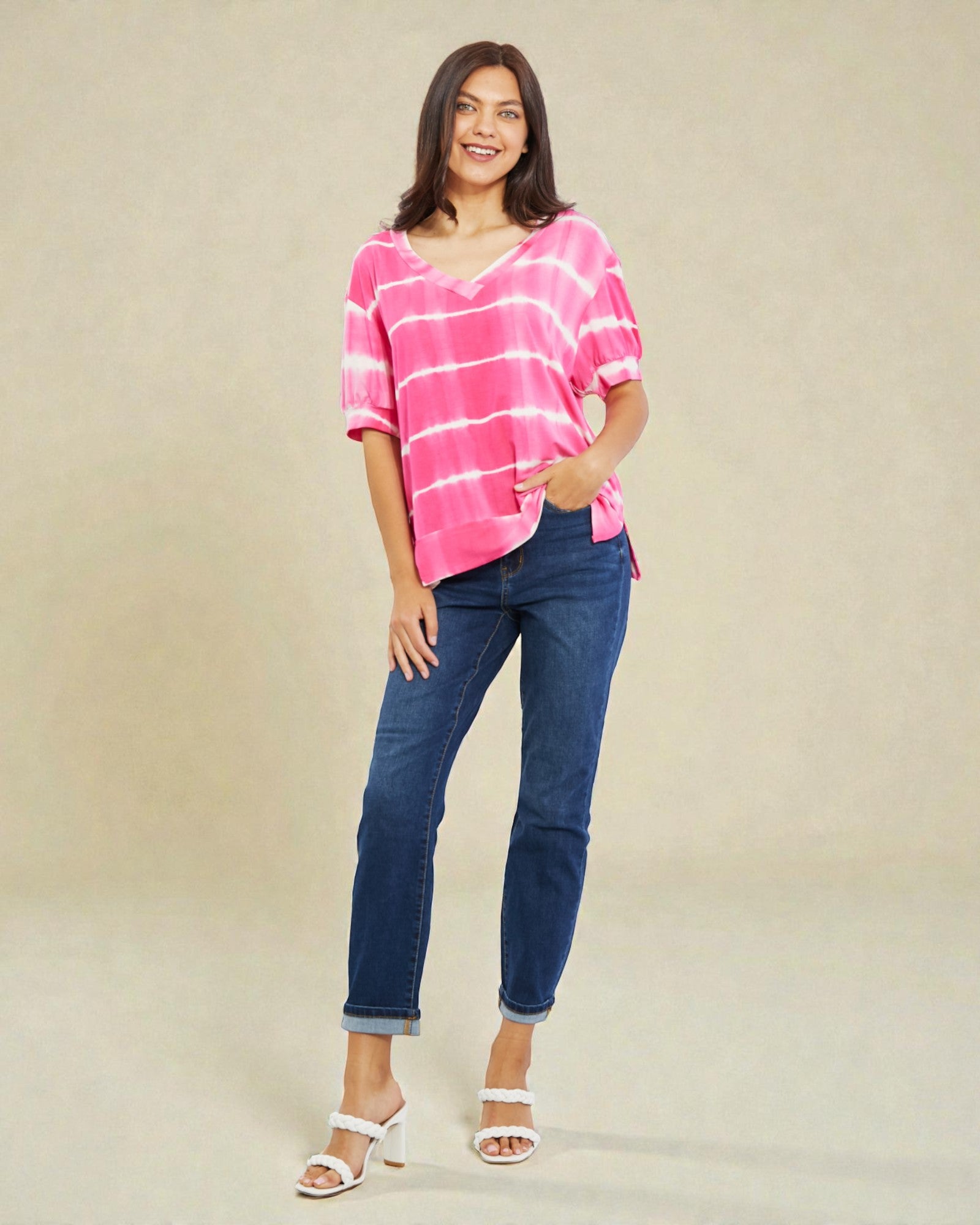 Woman wearing a pink striped shirt and blue jeans on a beige background