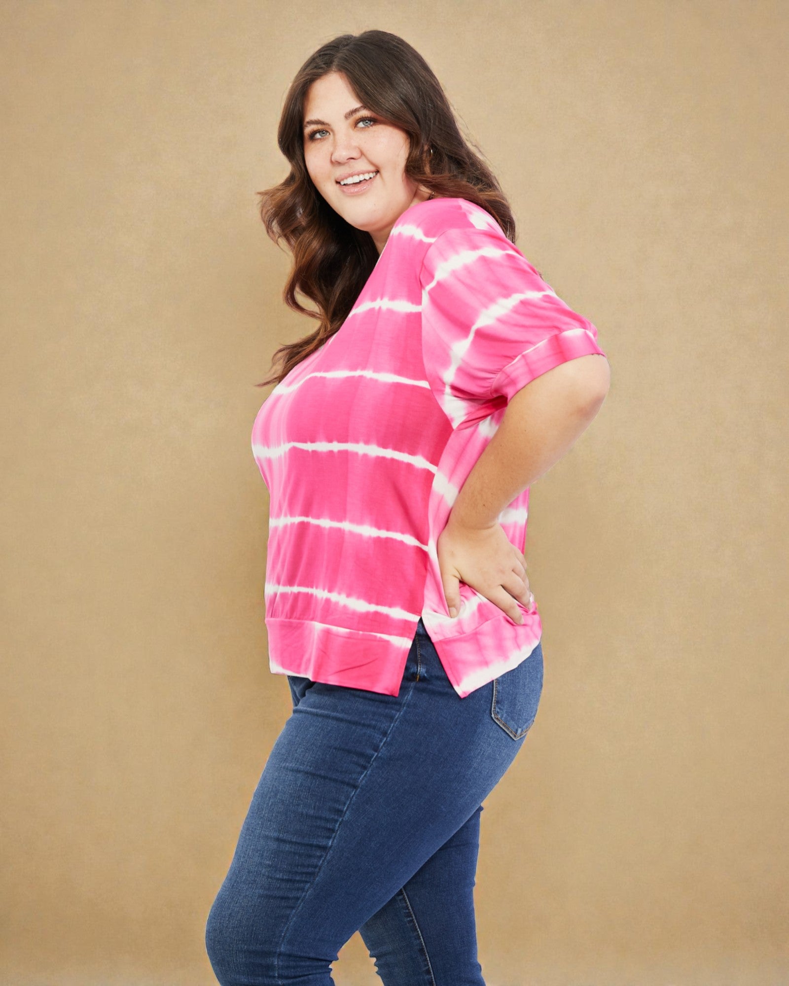 Woman wearing a pink tie-dye shirt and blue jeans against a beige background