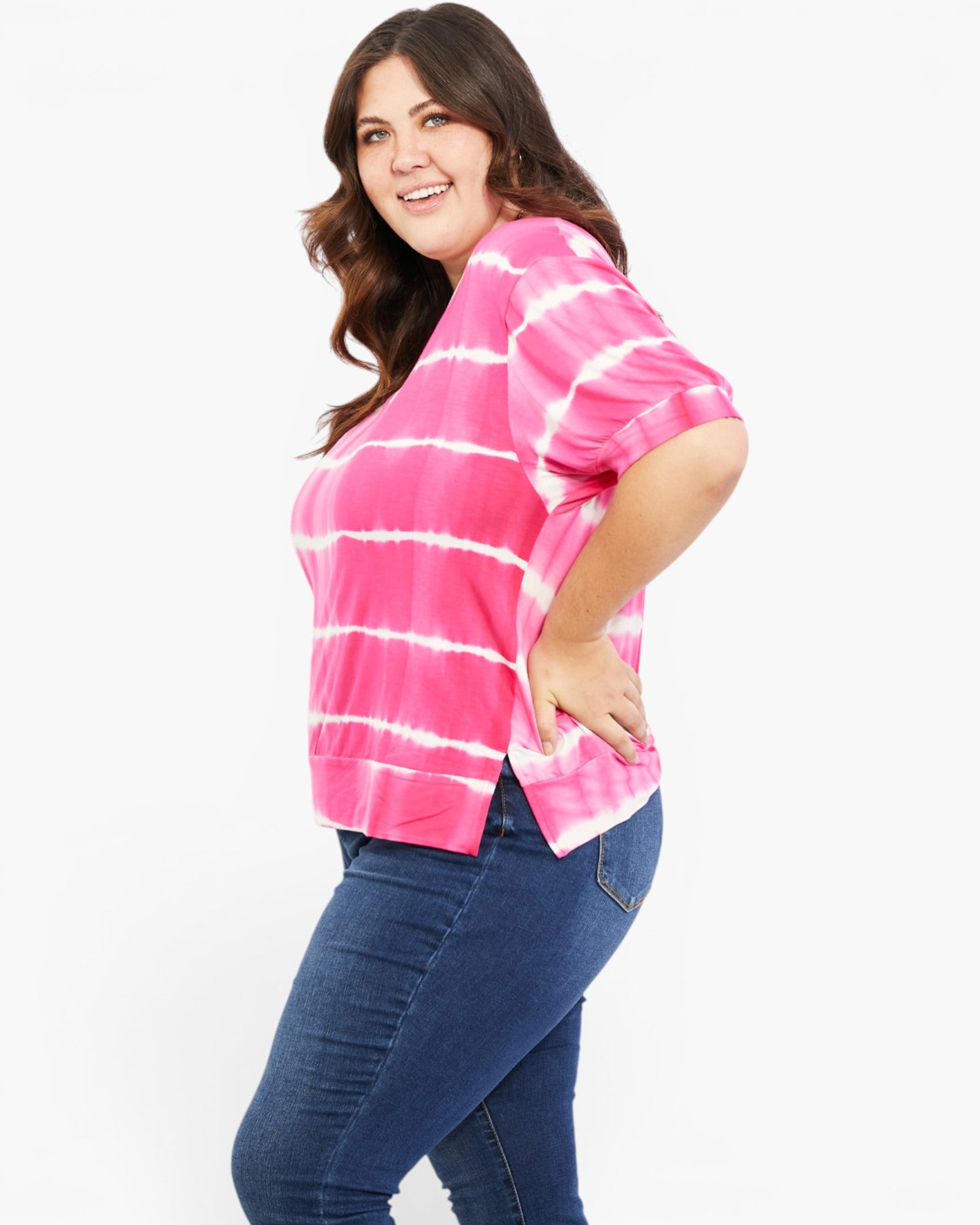 A woman modeling a pink and white tie-dye short-sleeve top with blue jeans against a plain white background.