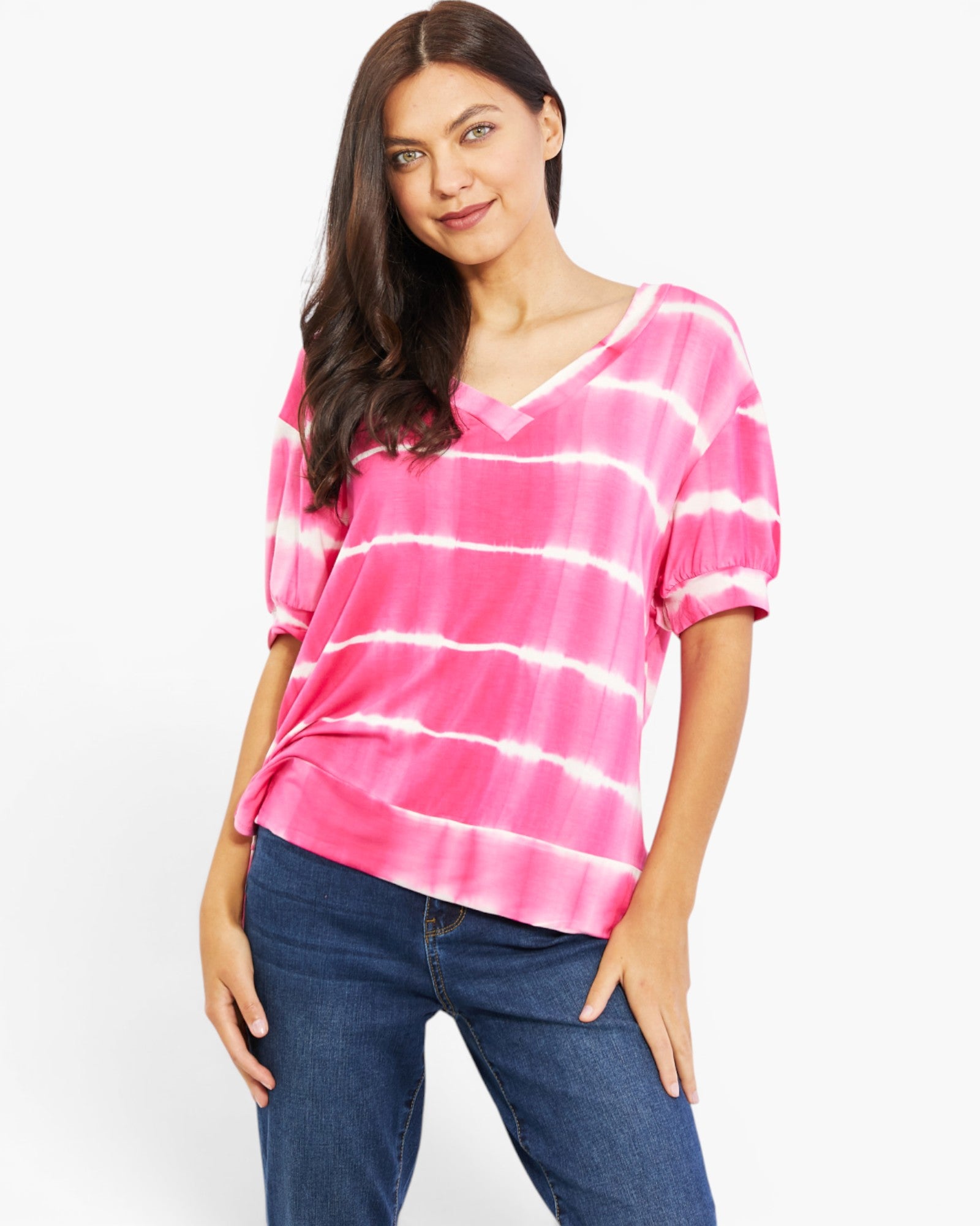 A woman modeling a pink and white tie-dye short-sleeve top with a V-neckline, paired with dark blue jeans, against a plain white studio background.