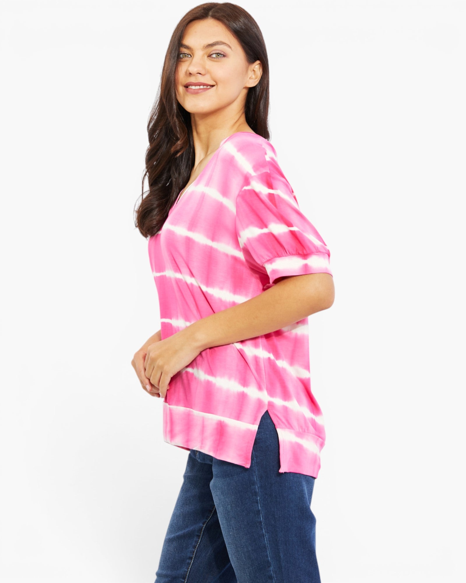 A woman wearing a pink and white tie-dye short-sleeve top with blue jeans, photographed against a plain white studio background.