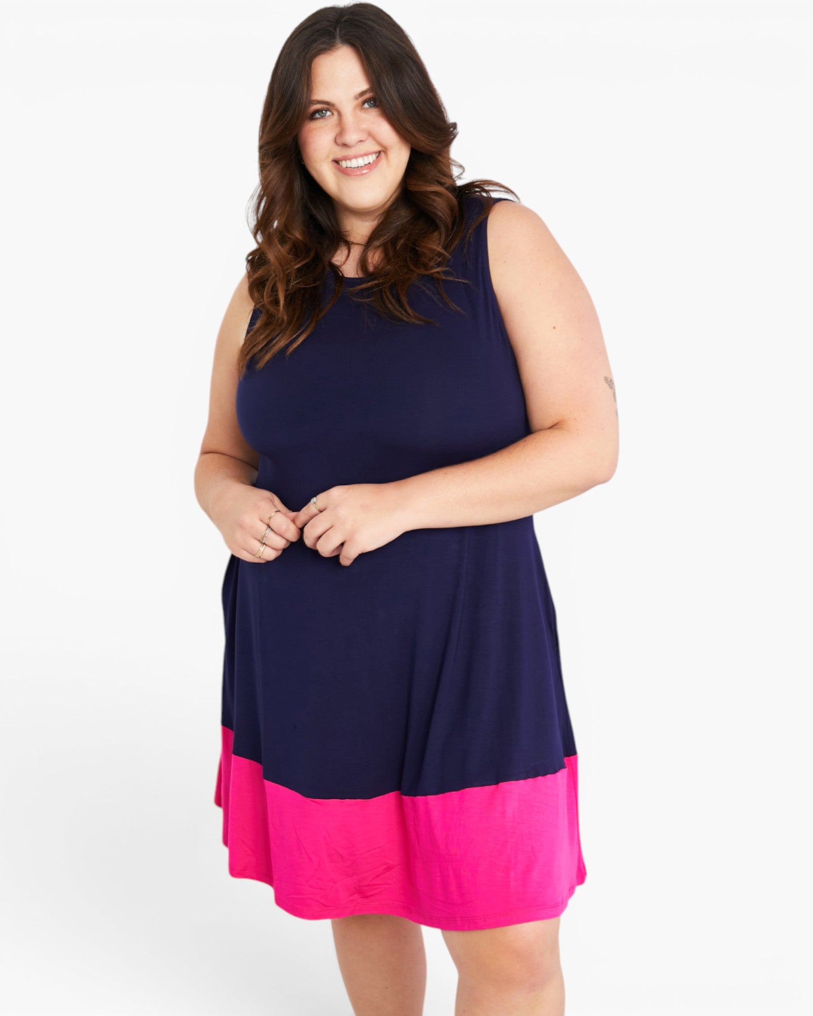 A woman modeling a sleeveless A-line dress with a navy blue upper section and a bright pink hem, set against a plain white studio background.