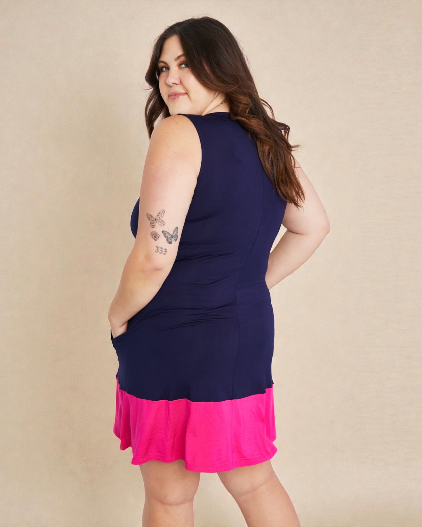 Woman wearing a navy sleeveless top with a pink skirt on a beige background
