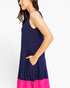 A woman wearing a sleeveless navy blue dress with a bright pink hem, shown from a side profile against a plain white background.