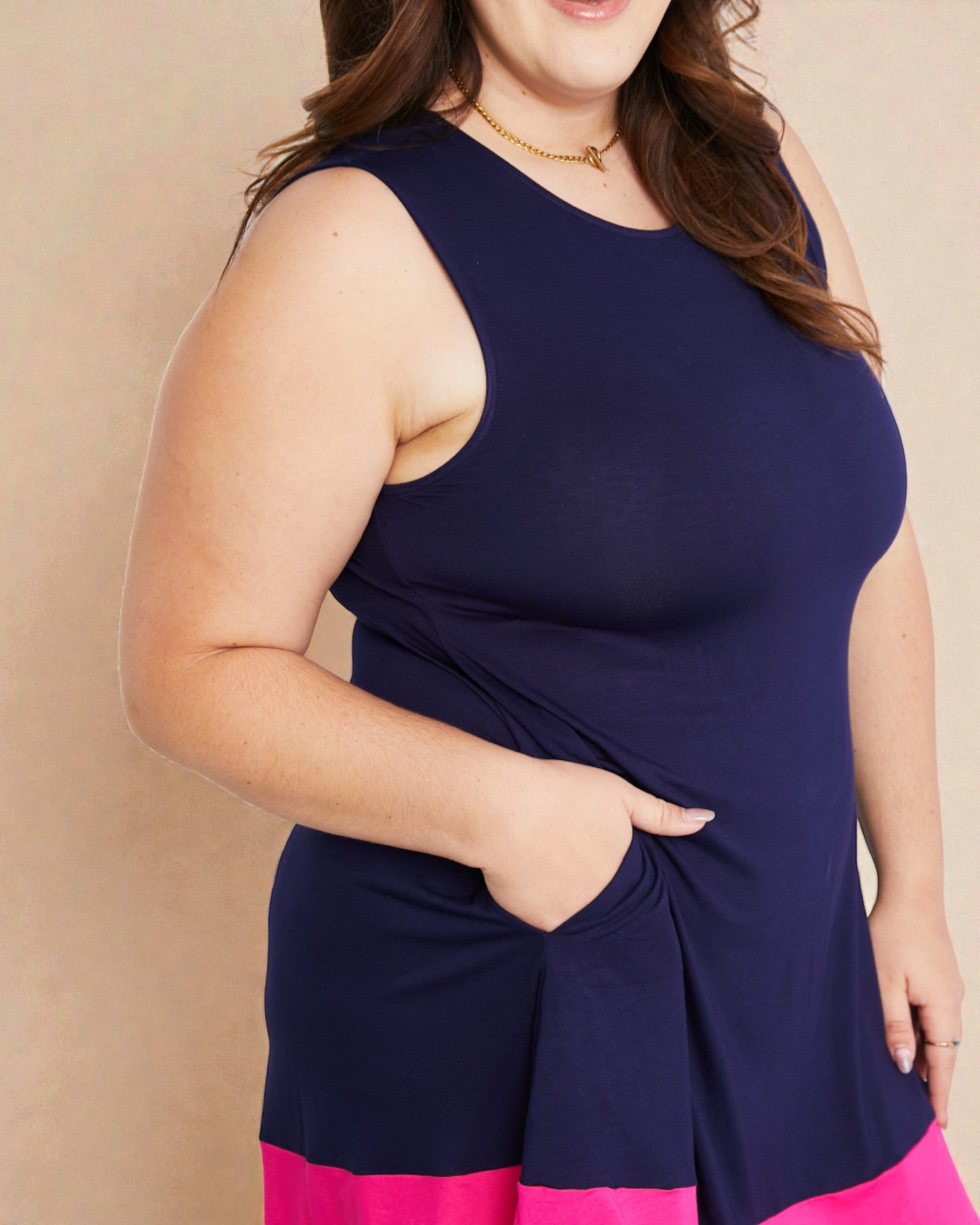 Woman wearing a navy blue sleeveless top with pink bottom against a beige background