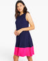 A woman modeling a sleeveless colorblock dress with a navy blue upper section and a bright pink flared hem, set against a plain white studio background.