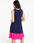 A woman shown from the back wearing a sleeveless A-line dress with a dark navy blue upper section and a bright hot pink flared hem, set against a plain white studio background.